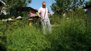 Pembe tişörtlü bir adam elektrikli tırpanla çimleri biçer.