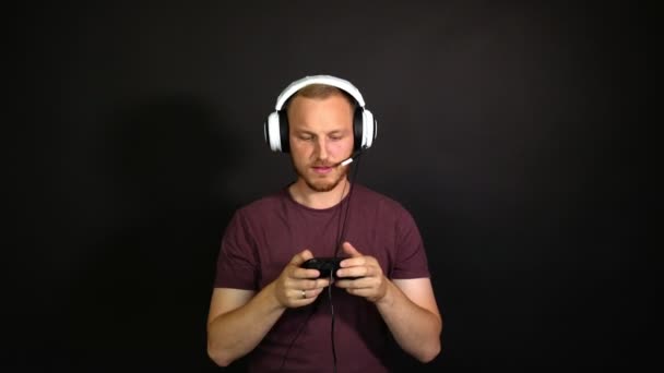 Fröhlicher Bärtiger Mann Setzt Kopfhörer Auf Nimmt Ein Gamepad Und — Stockvideo