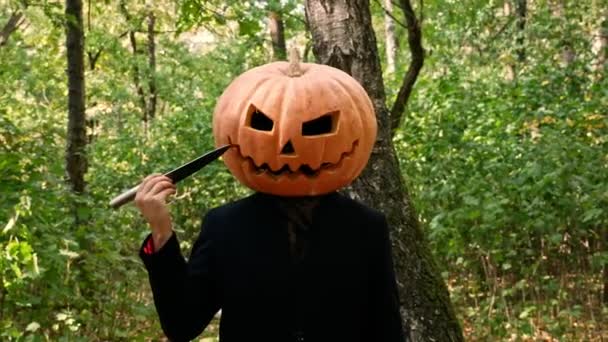 ジャック パンプキンヘッドは森の中に立ち 顔の近くにナイフを持って手探りで立っている 男は彼の頭の上に本物のカボチャを置きます ハロウィーンのコンセプト — ストック動画