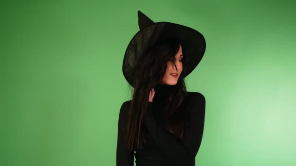 黒と魔女の帽子をかぶった若い美しい女性がカメラを見て微笑む ハロウィーン — ストック動画