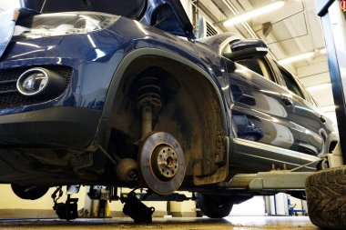 Tamir için kaldırılan modern lüks bir araba. Aracın ön tekerleği sökülmüş ve sürücü mili sökülmüş. Servis ve onarım, yedek parça kavramı.