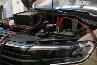 Araç servisindeki modern bir araba teşhis noktasında. Aracın kaputu açık ve teşhis cihazları bağlı..