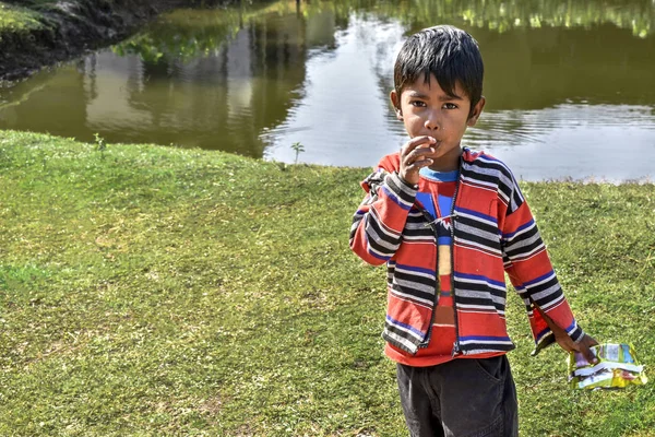 Um pobre rapaz inocente da Índia a comer batatas fritas e a olhar para a câmara — Fotografia de Stock