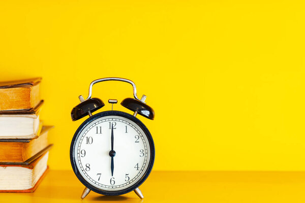 Alarm clock and book on yellow background with copy space.