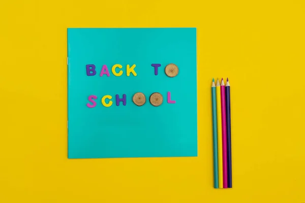 Texte de retour à l'école sur un bloc-notes avec crayons de couleur à côté sur fond jaune orangé . — Photo