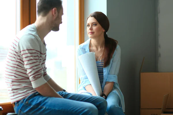 Young couple sitting on the floor and looking at the blueprint of new home. Young couple — Stock Photo, Image