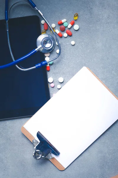 Sprzęt medyczny: niebieski stetoskop i tabletki na szarym tle. — Zdjęcie stockowe