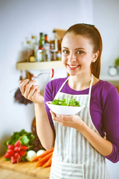 Jonge vrouw die het eten van verse salade in de moderne keuken. Jonge vrouw in de keuken — Stockfoto