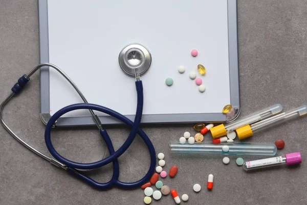 Sprzęt medyczny: niebieski stetoskop i tabletki na szarym tle. — Zdjęcie stockowe