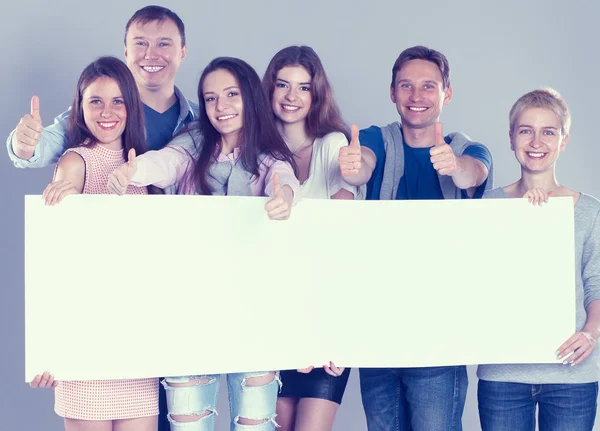 Young group of people standing together, holding a blank and showing ok — Stock Photo, Image