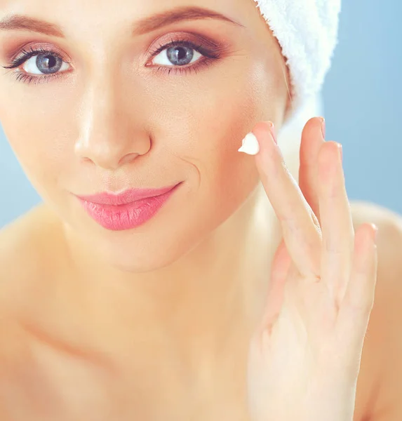 Beautiful young woman applying a creme on her face isolated on gray background — Stock Photo, Image
