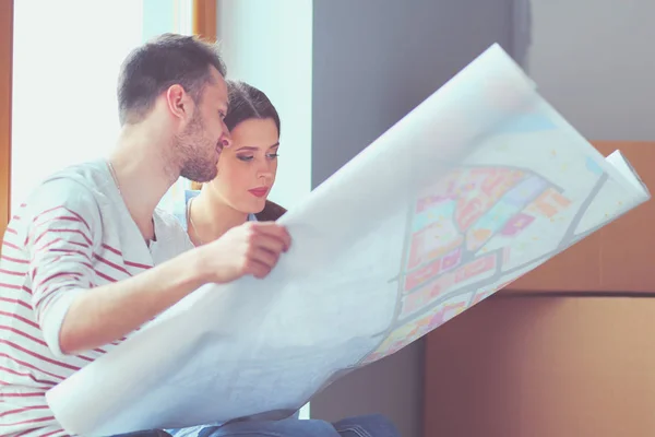 Jong (echt) paar zittend op de vloer en kijken naar de blauwdruk van de nieuwe woning. Jong koppel — Stockfoto