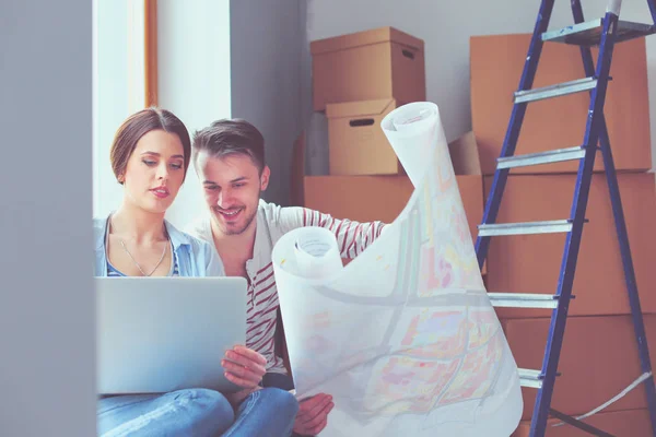 Jong (echt) paar zittend op de vloer en kijken naar de blauwdruk van de nieuwe woning. Jong koppel — Stockfoto