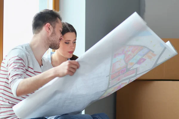 Jong (echt) paar zittend op de vloer en kijken naar de blauwdruk van de nieuwe woning. Jong koppel — Stockfoto