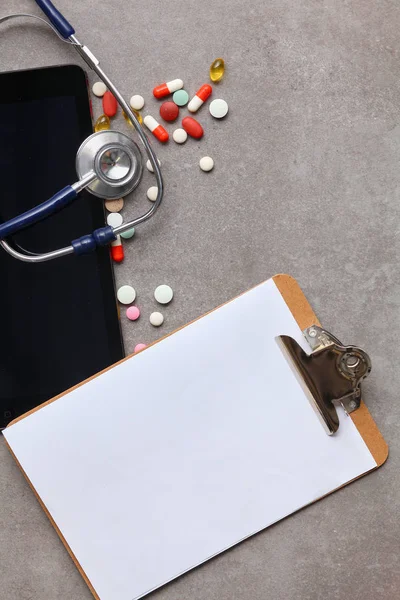 Medical equipment: blue stethoscope and tablet on gray background.