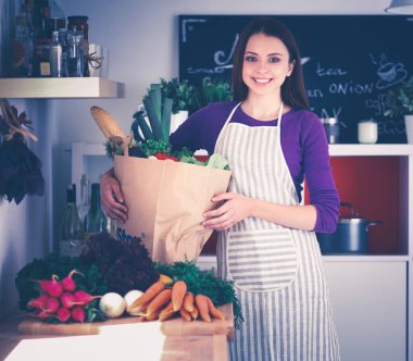 Mutfakta elinde bir torba erzakla duran genç bir kadın..