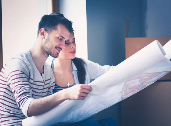 Jong stel zit op de vloer en kijkt naar de blauwdruk van een nieuw huis — Stockfoto