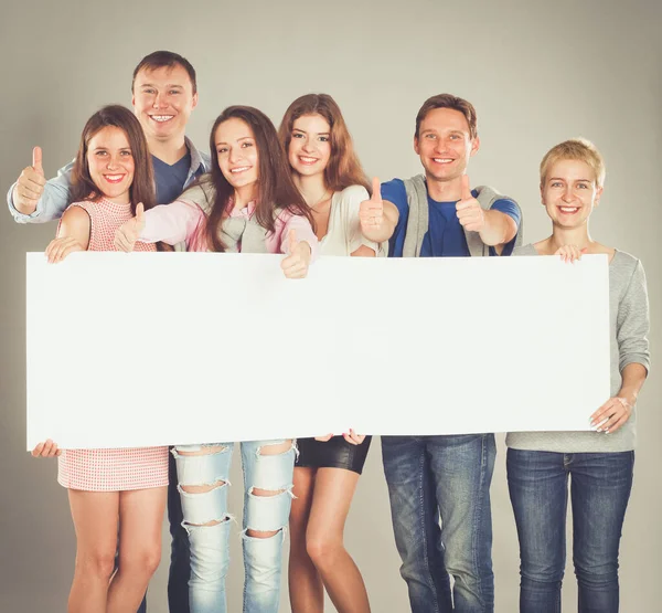 Young group of people standing together, holding a blank and showing ok — Stock Photo, Image