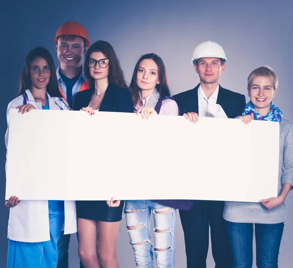 Grupo feliz de pessoas de diferentes profissões segurando um cartaz em branco. — Fotografia de Stock