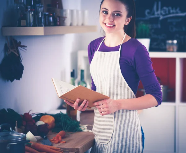 Mujer joven leyendo libro de cocina en la cocina, buscando receta —  Fotos de Stock