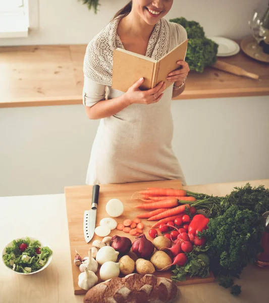 Jonge vrouw die kookboek leest in de keuken, op zoek naar recept — Stockfoto