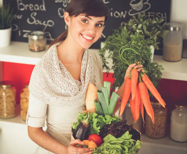 Feliz joven sosteniendo racimo de zanahorias en la cocina —  Fotos de Stock