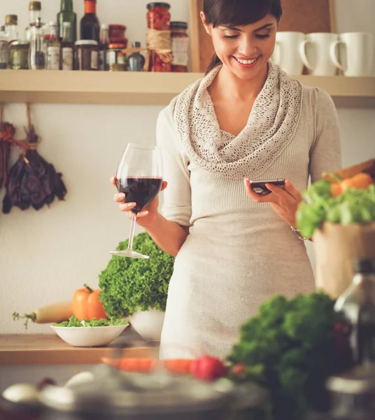 Junge Frau schneidet Gemüse in Küche und hält ein Glas Wein in der Hand — Stockfoto