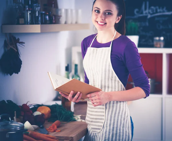 Jonge vrouw die kookboek leest in de keuken, op zoek naar recept Stockafbeelding