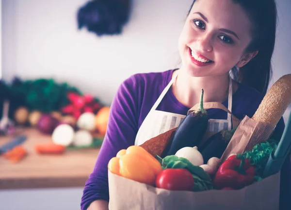 Een jonge vrouw in haar keuken met een zak boodschappen.. Stockafbeelding