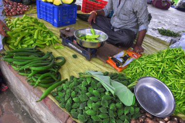 Yaşlı bir Hint vatandaşı pazarda sebze ticareti yapıyor. Bir adam yeşil biber ağırlığındadır.