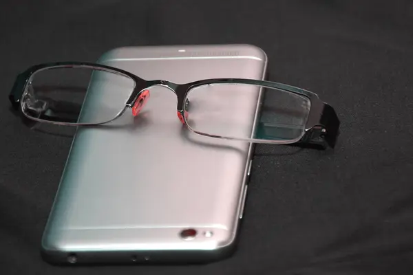 Platt låg foto av svart duk med smartphone och glasögon — Stockfoto