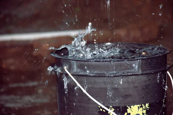 Rainy weather on the terrace in summer. The rain falls into the bucket and creates splashes