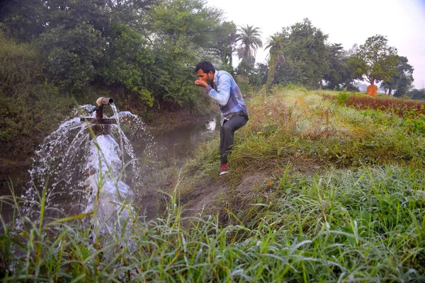 Agricultural equipment for field irrigation, an Indian farmer drinking water from water jet overflowing on his farm, Rain fog, selective focus