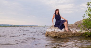 Nehrin yanında bir kayaya oturan uzun siyah elbiseli Genç çekici kız.