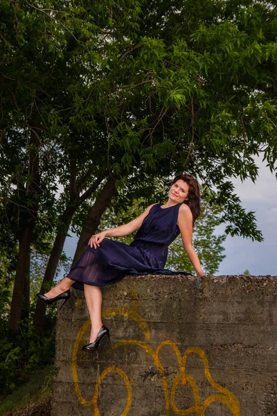 Bir taş parapetin üzerinde oturan siyah elbiseli kız