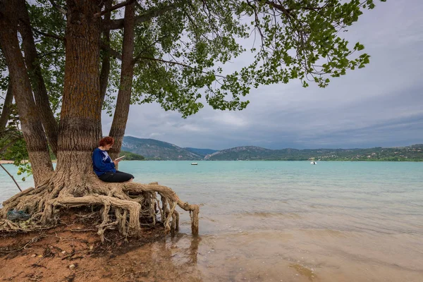 bir gölün kıyısında bir ağaçta oturan kadın okuma