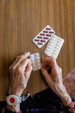 Yaşlı kadın bileğinde tıbbi uzaktan yardım düğmesiyle haplarını hazırlıyor.