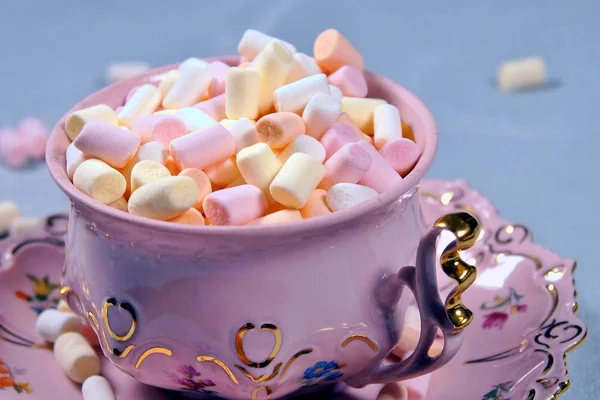 little White Fluffy white and pink marshmallows in floral pink and golden Porcelain vintage tea cup. marshmallows using for roasting and hot chocolate. food background concept. light blue background.