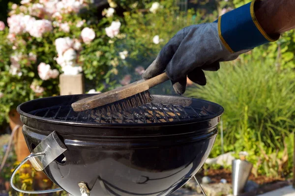 Cleaning a grill. Male hand with gloves cleans stiff brush round grill before cooking. man is cleaning a grill at garden.