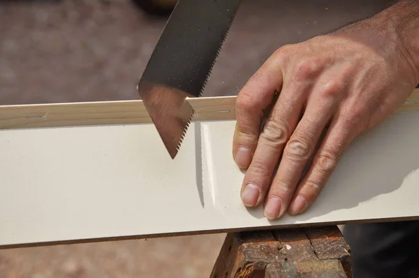 male worker hands sawing wood board using saw. detail, old carpenter hands at work with a saw.