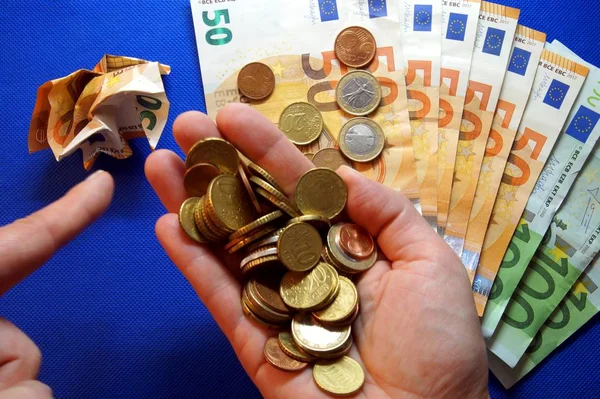 coins of euro in open hand and Hand finger pointing to a crumpled up Euro note