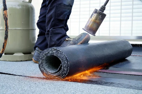 Flat roof installation with propane blowtorch during construction works with roofing felt. Heating and melting bitumen roofing felt. Roofing felt. Roofer working. Roofer working tool. Waterproofing