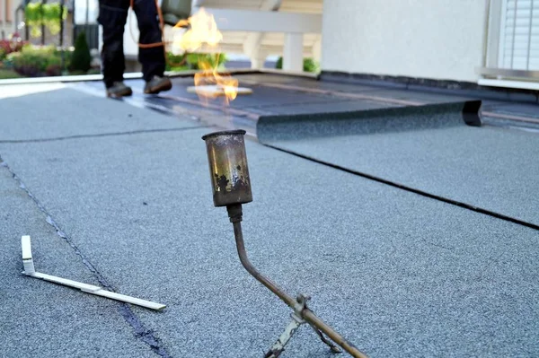 Flat roof installation with propane blowtorch during construction works with roofing felt. Heating and melting bitumen roofing felt. Roofing felt. Roofer working. Roofer working tool. Waterproofing