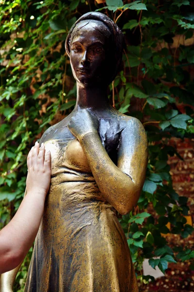 woman\'s hand is touching the bronze Statue of Juliet Capulet in her house backyard. Courtyard of Juliet\'s house in Verona, Veneto, italy