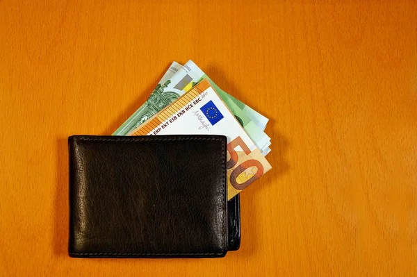leather wallet with a pile of euro, finance currency isolated on wooden background. banknotes 100 and 50 euros in a man\'s leather purse. Top view Men\'s wallet with cash euro.