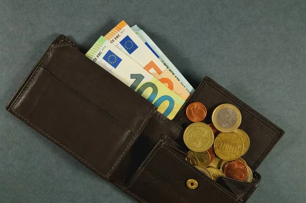 leather wallet with a pile of euro banknotes and euro money cash coins, finance currency isolated, dark background. coins and banknotes 100 and 50 euros in a man\'s leather purse. Top view Men\'s wallet