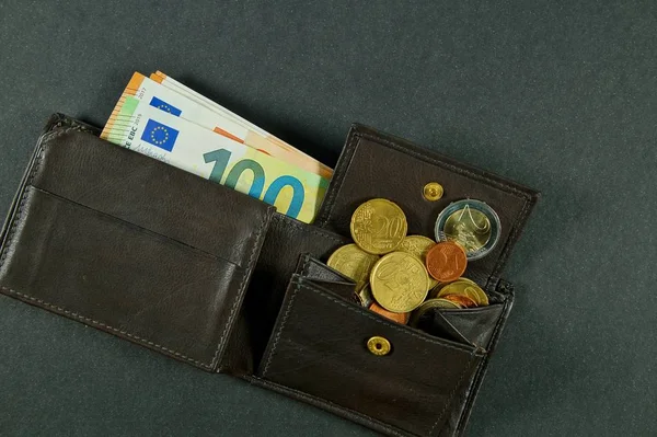 leather wallet with a pile of euro banknotes and euro money cash coins, finance currency isolated, dark background. coins and banknotes 100 and 50 euros in a man\'s leather purse. Top view Men\'s wallet