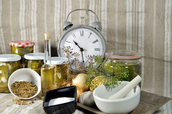 time to pickled. to keep long time. Pickled cucumbers in glass jar with clock, herbs and dill spices, on a fabric linen background. Natural products ready for winter. organic and healthy meal concept.