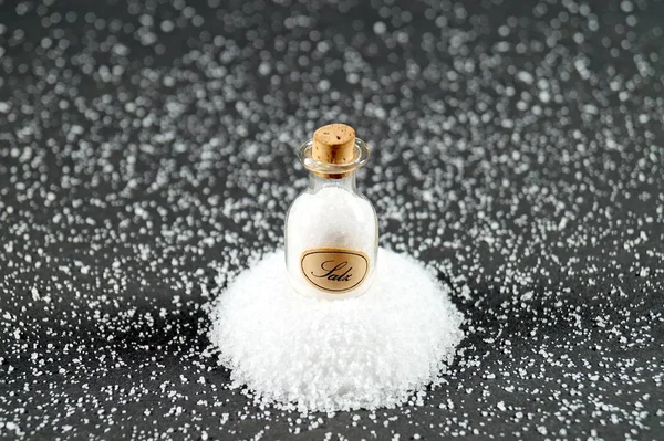 Crystals of shallow salt. old vintage german Salz Miniature glass salt shaker on a dark gray black table. Background for advertising salt. Table salty. Salted food. A pile / heap of salt. concept excessive salt intake. spilled salt on dark background