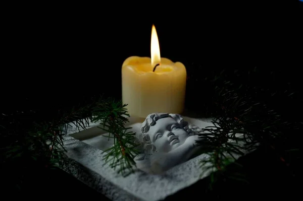 Guardian angel, Fir branches with a burning candle on black background. Christmas tree branches and an Angel lying on the table against darkness. Condolence card concept in christmas time or New year. Funeral symbol.